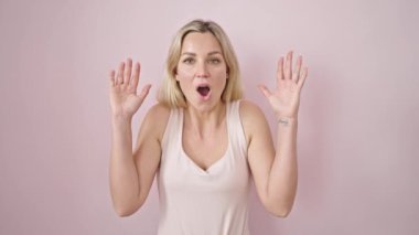 Young blonde woman standing with surprise expression over isolated pink background