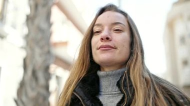 Genç beyaz kadın gülümsüyor. Sokakta kendine güveni tam.