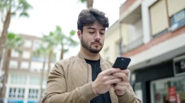 Genç İspanyol adam sokakta gülümseyen akıllı telefon kullanıyor.