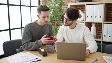 Ofiste çalışan bilgisayar ve akıllı telefon kullanan iki erkek iş ortağı.
