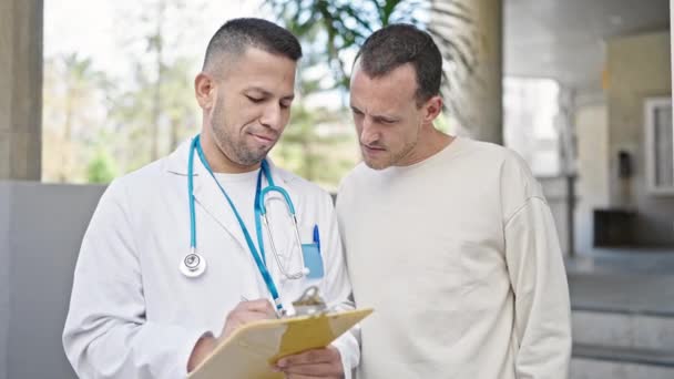 Dos Hombres Doctor Paciente Teniendo Informe Médico Escritura Consulta Hospital — Vídeo de stock
