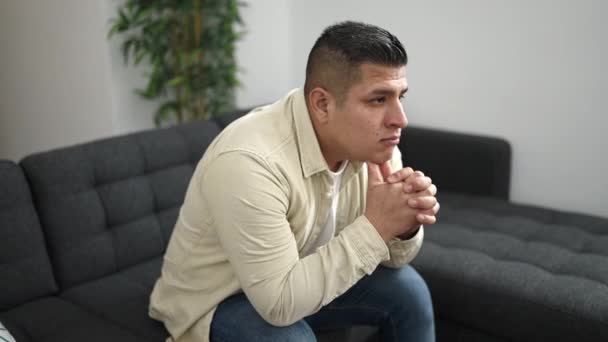 Νεαρός Ισπανός Που Φαίνεται Σκεπτικός Καθισμένος Στον Καναπέ Στο Σπίτι — Αρχείο Βίντεο