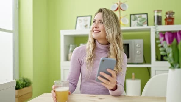 Νεαρή Ξανθιά Γυναίκα Πίνοντας Ποτήρι Χυμό Πορτοκαλιού Χρησιμοποιώντας Smartphone Στην — Αρχείο Βίντεο