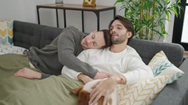 İki erkek birbirini kucaklıyor. Kanepede köpek ile dinleniyorlar.