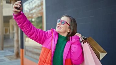 Beyaz saçlı, gülümseyen olgun bir İspanyol kadın. Elinde çantalarla alışverişe gidiyor. Sokakta selfie çekiyor.