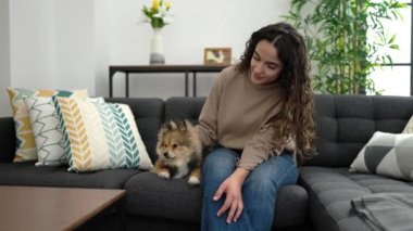 Köpeğiyle gülümseyen genç İspanyol kadın evdeki kanepede oturuyor.