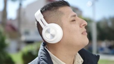 Genç İspanyol adam parkta müzik dinliyor.
