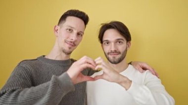 İki erkek birbirlerine sarılıp, izole edilmiş sarı arka planda kalp hareketi yapıyorlar.