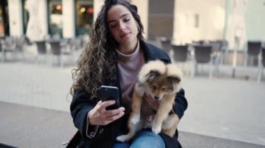 Köpekli genç İspanyol kadın gülümsüyor. Kendine güveni tam. Sokakta akıllı telefondan selfie çekiyor.