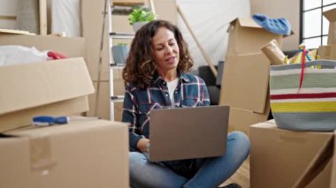 Orta yaşlı İspanyol kadın yeni evinde dizüstü bilgisayar kullanıyor.