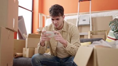 Genç İspanyol adam video oynuyor. Yeni evine üzgün bakıyor.
