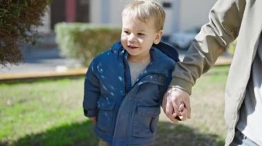 Baba oğul gülümsüyor. Parkta el ele yürüyorlar.