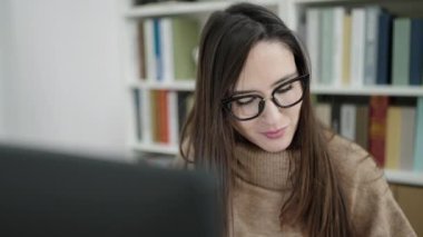 Kütüphanede bilgisayar kullanarak kurabiye yiyen güzel İspanyol kadın öğrenci.
