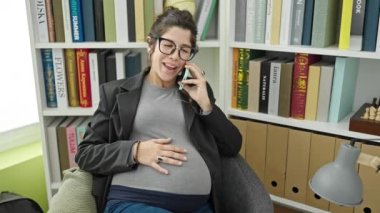 Genç hamile kadın öğretmen gülümsüyor kütüphane üniversitesinde akıllı telefondan konuşuyor.