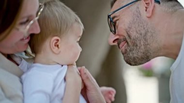 Anne, baba ve bebeğin ailesi parkta birlikte gülümsüyor.