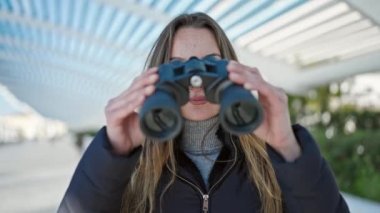 Genç beyaz kadın parkta dürbün kullanıyor.