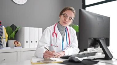 Genç beyaz kadın doktor klinikte bilgisayar kullanıyor.