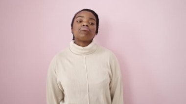 İzole edilmiş pembe arka planda üzgün bir ifadeyle duran Afrikalı Amerikalı kadın.