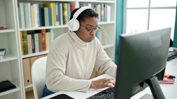 アフリカ系アメリカ人の女性が図書館大学でコンピューターとヘッドフォンを使って学ぶ — ストック動画