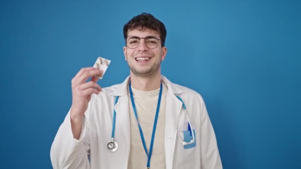 年轻的惊慌失措的医生在孤立的蓝色背景下吃药 — 图库视频影像