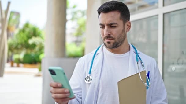 Jovem Hispânico Homem Médico Segurando Relatório Médico Usando Smartphone Hospital — Vídeo de Stock