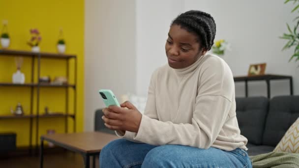Afroamerikanerin Sitzt Mit Smartphone Hause Auf Sofa — Stockvideo