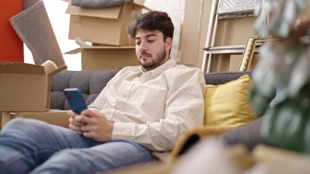 Jovem Hispânico Usando Smartphone Sentado Sofá Uma Nova Casa — Vídeo de Stock