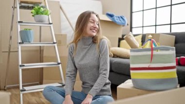 Beyaz bir kadın yeni evinde yerde oturmuş dans ediyor.