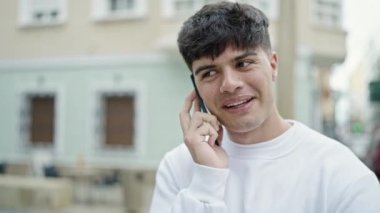 Genç İspanyol adam akıllı telefondan konuşuyor. Sokakta gülümsüyor.