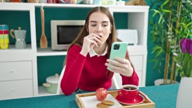 Genç İspanyol kadın kahvaltı yapıyor. Yemek odasında akıllı telefon kullanıyor.