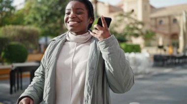 Parkta akıllı telefondan müzik dinleyen Afrikalı Amerikalı kadın.