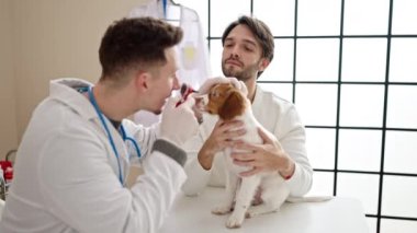 Veteriner kliniğinde köpeğin gözlerini inceleyen iki adam.