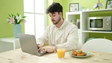 Genç İspanyol kahvaltı yapıyor. Yemek odasında dizüstü bilgisayar kullanıyor.