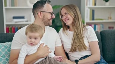 Anne, baba ve bebeğin ailesi evdeki kanepede otururken gülümsüyor.