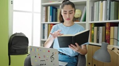 Kütüphanede dizüstü bilgisayar kullanarak kitap okuyan güzel İspanyol bir kadın öğrenci.