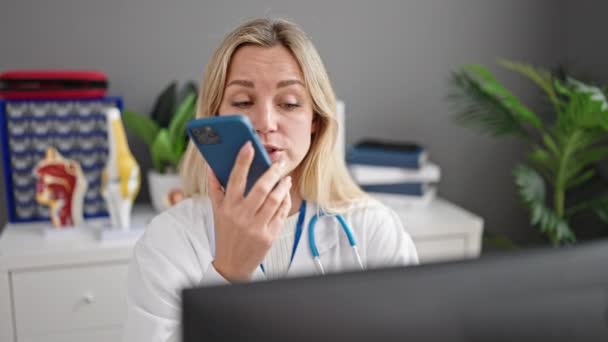 若いブロンド女性医師使用コンピュータ送信音声メッセージによるスマートフォンによってクリニック — ストック動画