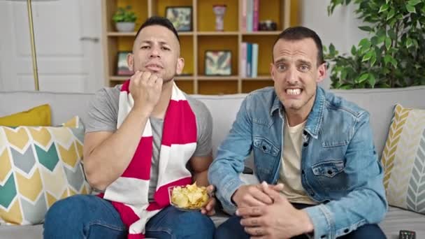 Dwóch Mężczyzn Wspierających Drużynę Piłkarską Siedzącą Kanapie Wyglądającą Zdenerwowaną Domu — Wideo stockowe