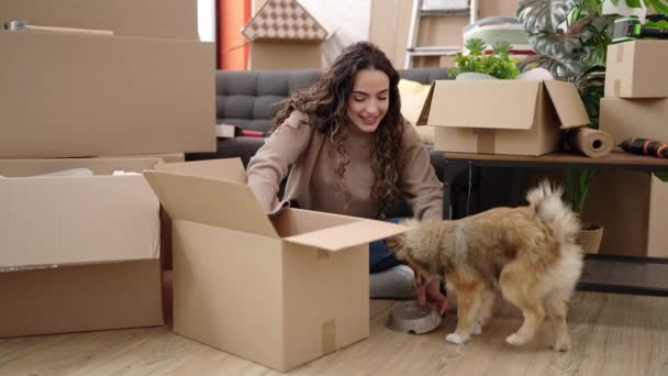 Jonge Spaanse Vrouw Met Hond Uitpakken Kartonnen Doos Zittend Vloer — Stockvideo