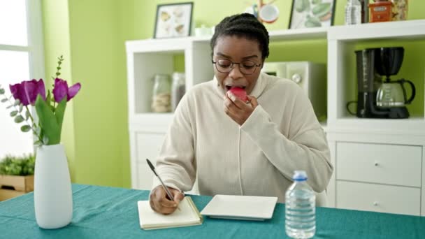 Afroamerikanerin Schreibt Auf Notizbuch Und Isst Apfel Esszimmer — Stockvideo
