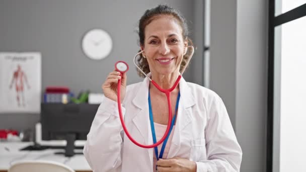 Middle Age Hispanic Woman Doctor Smiling Confident Holding Stethoscope Clinic — ストック動画