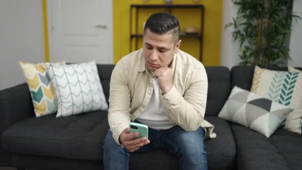 Young Hispanic Man Using Smartphone Sitting Sofa Looking Upset Home — Stock Video