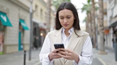 Genç ve güzel İspanyol kadın akıllı telefon kullanıyor. Sokakta ciddi bir ifadesi var.