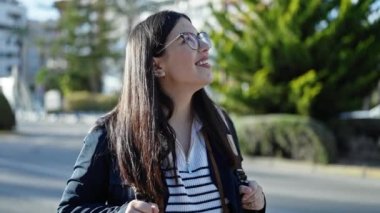 Sırt çantalı ve gülümseyen kameralı genç İspanyol kadın turist sokağa bakıyor.