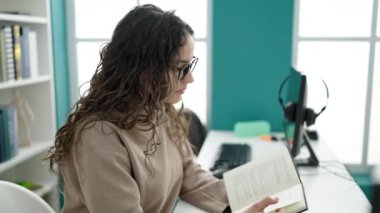 Young beautiful hispanic woman student reading book doing silence gesture at library university