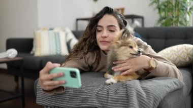 Köpekli İspanyol bir kadın akıllı telefonuyla evdeki kanepede selfie çekiyor.
