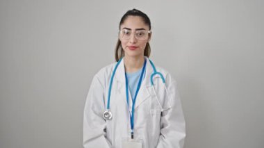 Kollarını kavuşturmuş genç ve güzel İspanyol kadın doktor, kafası soyutlanmış beyaz arka planda, hayır diyor.