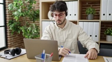 Genç Hispanik adam çağrı merkezi ajanı ofiste notlar yazıyor.