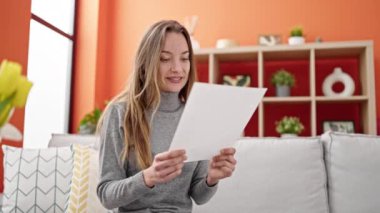 Beyaz bir kadın gülümsüyor. Evinde kendinden emin bir şekilde kitap okuyor.
