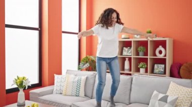 Orta yaşlı İspanyol kadın gülümseyerek evdeki kanepede dans ediyor.