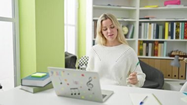 Genç sarışın kız öğrenci kütüphanede baterist olarak kalem kullanıyor.